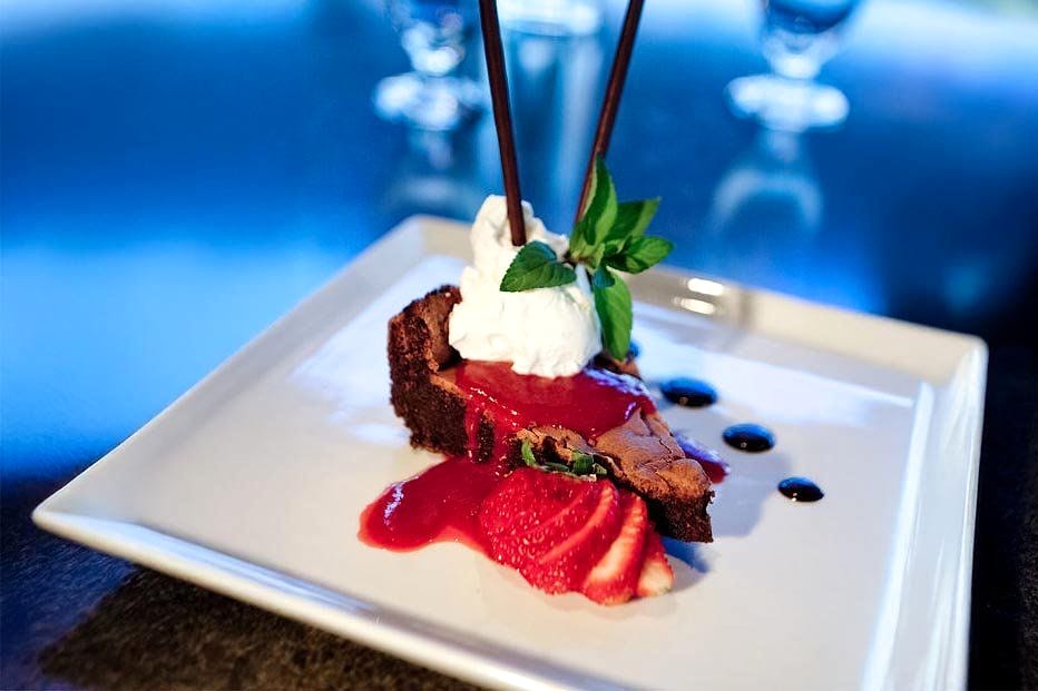 Chocolate tart dessert with strawberry sauce, whipped cream and mint, plated on a white square plate