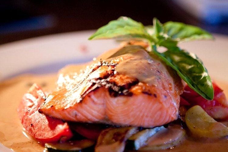 Grilled salmon fillet with basil garnish over roasted vegetables