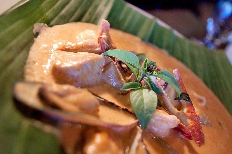 Crab in creamy curry sauce served on a banana leaf with fresh herb garnish