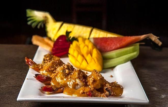 Breaded shrimp with peanut sauce on a white plate, garnished with carved fruit